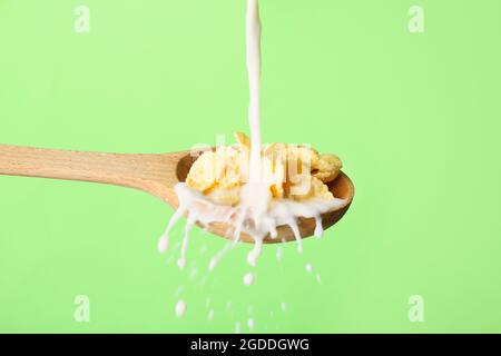 Gießen von Milch in Löffel mit Cornflakes auf farbigem Hintergrund, Nahaufnahme Stockfoto