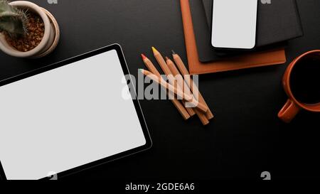 Wireless-Gerät auf Arbeitsplatz-Konzept, digitale Tablet-Modell und Smartphone-Modell mit Zubehör in schwarz und orange Farbe, schwarzer Hintergrund, oben V Stockfoto