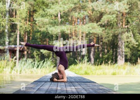 Eine Frau in Sportbekleidung, die im Park Yoga praktiziert, führt auf einer Matte eine Shirshasana-Übung mit einem Querfaden und Kopfstand durch Stockfoto