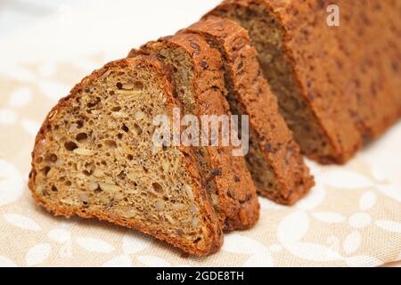 Frisches schwarzes Brot mit Sonnenblumenkernen, Leinsamen und Kürbiskernen, die auf einem Holzhintergrund in Stücke geschnitten wurden. Selektiver Fokus. Gesunde Lebensweise conce Stockfoto