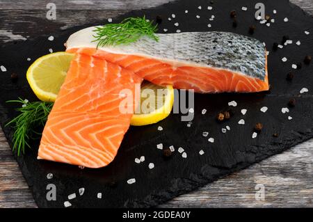 Zwei frische, rohe Lachsfilets mit Dillkräutergarnitur und Zitronenscheiben auf einem Schiefertafel Stockfoto