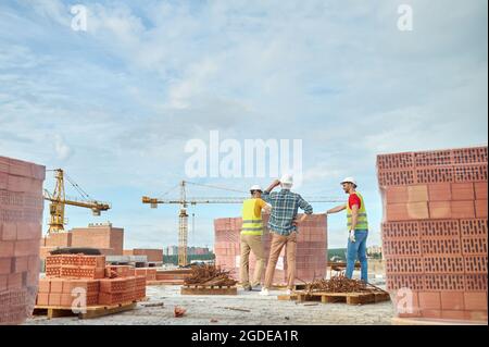 Drei Arbeiter in Harthüten prüfen die Qualität der roten Steine Stockfoto