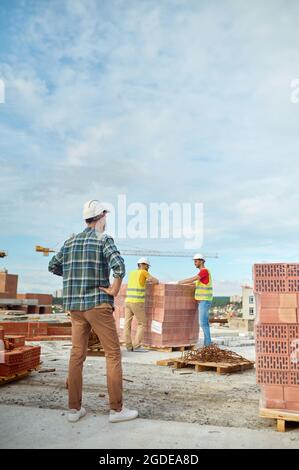 Vorarbeiter, der die Arbeit von zwei jungen Bauherren inspiziert Stockfoto