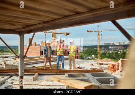 Drei Arbeiter in Hardhats bei einem Gespräch auf der Baustelle Stockfoto