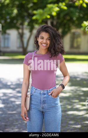 Lächelnde niedliche Mulatta in Jeans und rosa T-Shirt im Park Stockfoto