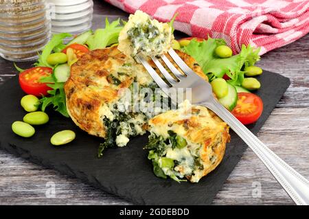 Spinat und Grünkohl-Quiche mit frischem Salat und Edamame-Bohnen auf einem Schieferbrett Stockfoto