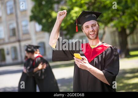 Groß glücklich Graduate SMS und schauen aufgeregt Stockfoto