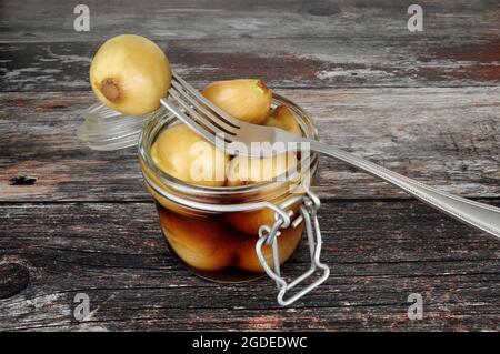 Glas-Vorratsglas gefüllt mit eingelegten Zwiebeln in Malzessig auf einem rustikalen Holzhintergrund Stockfoto