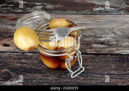 Glas-Vorratsglas gefüllt mit eingelegten Zwiebeln in Malzessig auf einem rustikalen Holzhintergrund Stockfoto