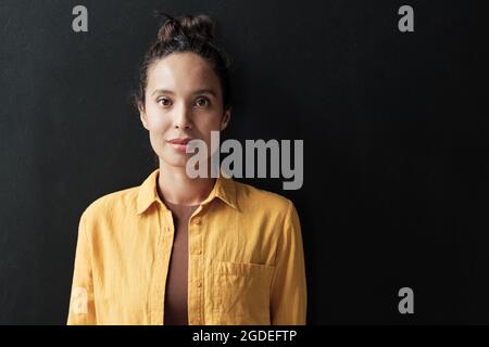 Porträt einer schönen jungen Frau, die vor dem schwarzen Hintergrund auf die Kamera schaut Stockfoto