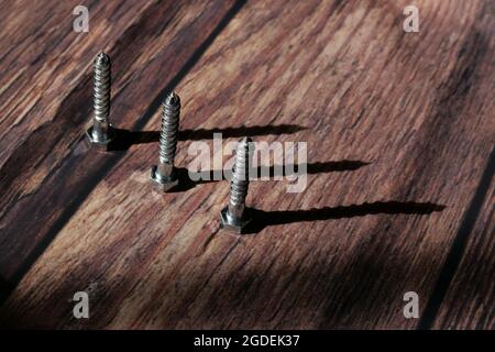 Drei silberne Schrauben stehen am Ende auf körnigem Holzhintergrund Stockfoto