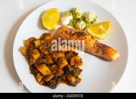 Gegrilltes Lachsfilet mit Spinat, Kartoffeln, Mozzarella in Nudelsoße und Zitrone Stockfoto