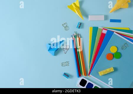 Notizbücher, Bleistifte, Farben, Spitzer, Büroklammern - Waren für die Schule, Büro auf blauem Hintergrund Stockfoto