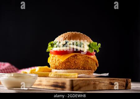 Knuspriger Hähnchenburger mit Käse und pommes auf einem Holztisch Stockfoto