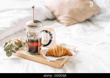 Auf weißem Bett, Croissant und Tee auf Korbtablett Stockfoto