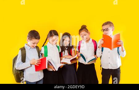 Fröhliche lächelnde kleine Studenten halten Farbbücher isoliert auf gelbem Hintergrund. Zurück zur Schule. Stockfoto