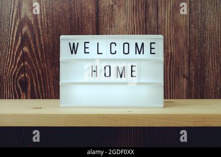 Welcome Home Word in einem Leuchtkasten auf Holzhintergrund Stockfoto