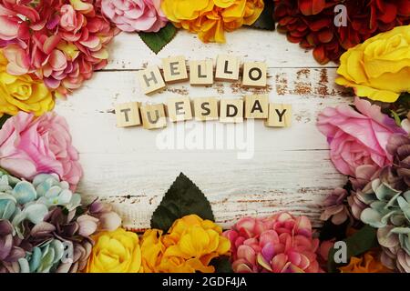 Der Buchstabe „Hello Tuesday“ mit farbenfrohem Blumenrahmen auf Holzhintergrund Stockfoto