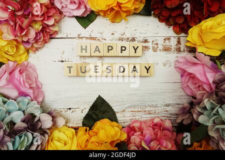 Der Buchstabe „Hello Tuesday“ mit farbenfrohem Blumenrahmen auf Holzhintergrund Stockfoto