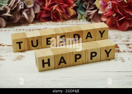 Der Buchstabe „Hello Tuesday“ mit farbenfrohem Blumenrahmen auf Holzhintergrund Stockfoto
