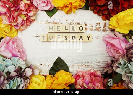 Der Buchstabe „Hello Tuesday“ mit farbenfrohem Blumenrahmen auf Holzhintergrund Stockfoto