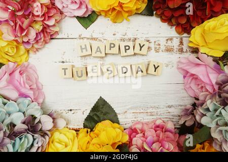Der Buchstabe „Hello Tuesday“ mit farbenfrohem Blumenrahmen auf Holzhintergrund Stockfoto