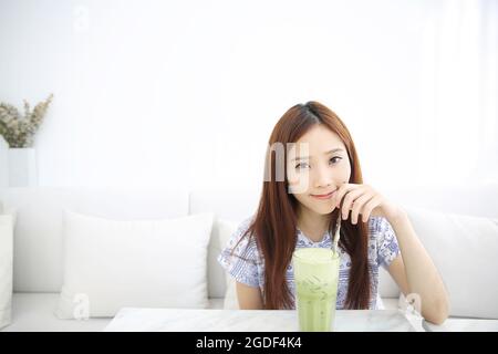 Asiatische junge Frau trinkt Iced Green Tea Latte in weißem Coffeeshop Stockfoto