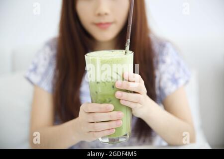 Asiatische junge Frau trinkt Iced Green Tea Latte in weißem Coffeeshop Stockfoto