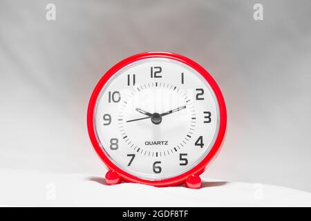 Kleiner roter Wecker zeigt die Laufzeit an. Eine moderne Uhr mit rotem Rahmen. Lächeln Sie das Gesicht einer Uhr. Nahaufnahme einer roten Plastikuhr mit einem zweiten Zeiger Stockfoto