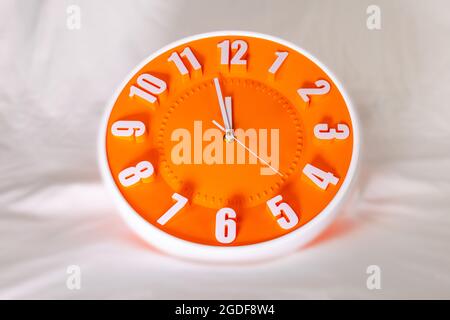 Das orangefarbene Ziffernblatt einer Wanduhr zeigt die Uhrzeit an. Es ist nahe bei 12 Uhr. Der neueste Bericht des Atomwissenschaftlers zeigt die Weltuntergangsuhr Stockfoto