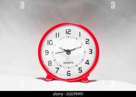 Kleiner roter Wecker zeigt die Laufzeit an. Eine moderne Uhr mit rotem Rahmen. Lächeln Sie das Gesicht einer Uhr. Nahaufnahme einer roten Plastikuhr mit einem zweiten Zeiger Stockfoto