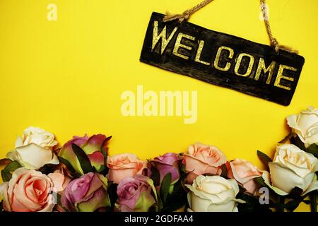 Begrüßungsschild mit Rosenblume auf gelbem Hintergrund Stockfoto