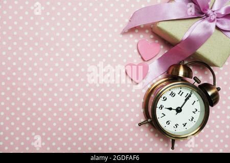 Wecker und Geschenkbox mit Rosenstrauß mit Raumkopie auf rosa Punktmuster Hintergrund Stockfoto