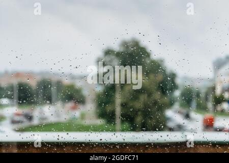 Regen fällt während Regen an regnerischen Tagen.Blick auf das Fenster, Glas mit verschwommenem Hintergrund.Wassertropfen fließt die Oberfläche hinunter.Nasses Glas, schlechtes Wetter Stockfoto