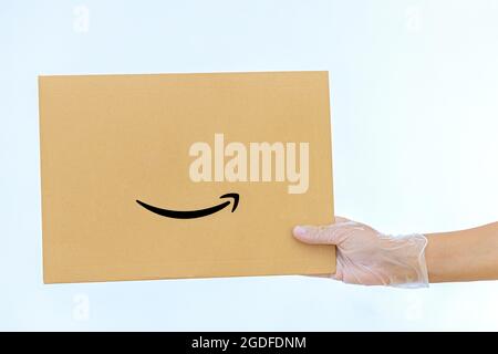 Eine Frau hält in medizinischen Handschuhen einen Papierumschlag Amazon auf weißem Hintergrund Expresslieferung der Kurier brachte das Paket mit Stockfoto