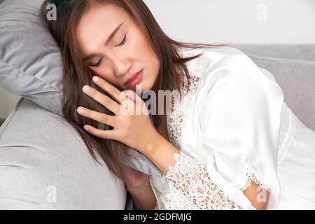 Asiatische Frau in einer Satin-Schlafkleidung weiß gesichert wegen Fieber und Fieber in der Nacht. Körpertemperatur Stockfoto