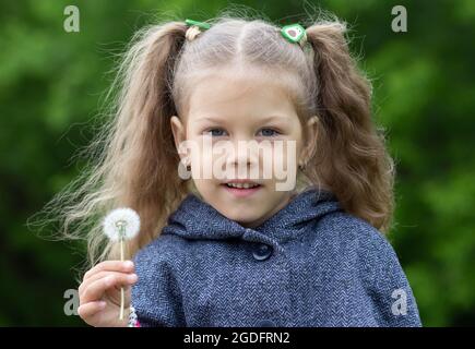 Portrat des kaukasischen Mädchens von fünf Jahren, das im Sommerpark in einer Hand den Dandelion hält Stockfoto