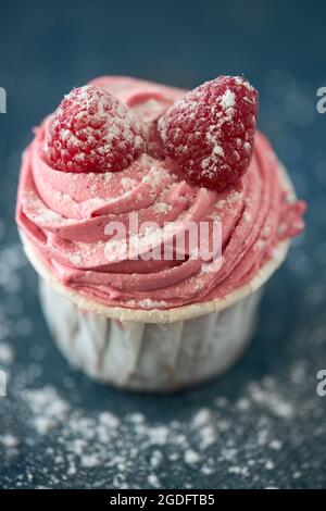 Nahaufnahme eines köstlichen rosa Cupcake mit Himbeeren isoliert auf blauem Hintergrund Stockfoto