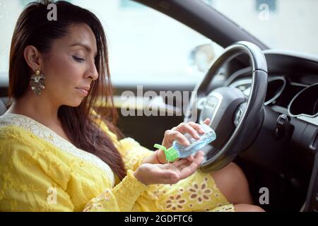 Porträt einer lateinischen Frau in einem gelben Kleid, die die Hände mit hydroalkoholischem Gel im Auto putzt Stockfoto