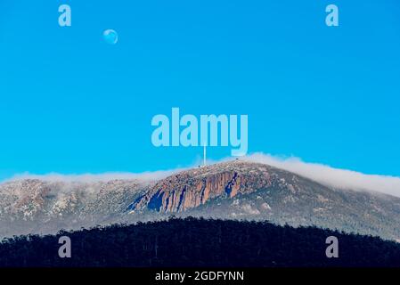 Mit dem Mond noch oben rollt eine Decke aus Wolken am frühen Morgen über Kunanyi (Mount Wellington) in Richtung Hobart, der Hauptstadt Tasmaniens in Australien Stockfoto