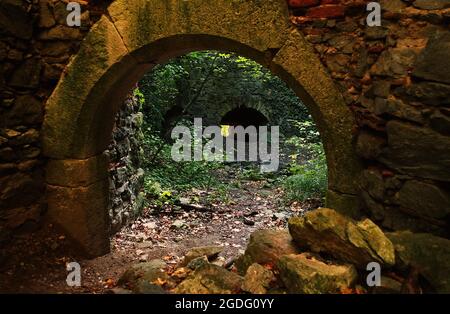 Im Inneren der alten historischen Ruinen von Schloss Scharfeneck mit einem Steinbogen und Steinen. In einer historischen Ruine. Eine verlassene Geisterburg im Wald. Stockfoto