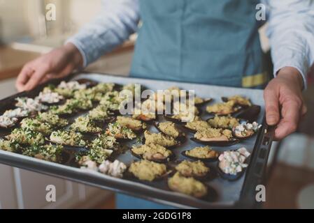 Koch hält das Blech mit gefüllten Muscheln vor dem Backen im Ofen. Stockfoto