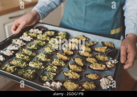 Koch hält das Blech mit gefüllten Muscheln vor dem Backen im Ofen. Stockfoto