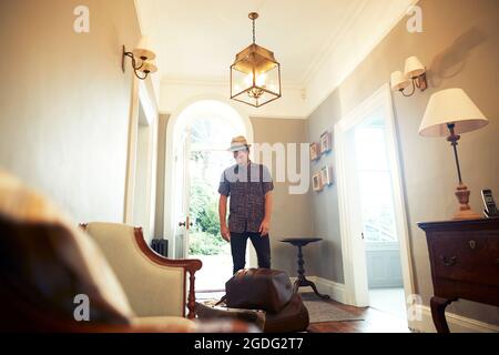 Junger Mann in Trilby Blick hinunter auf das Gepäck in der Lobby Stockfoto