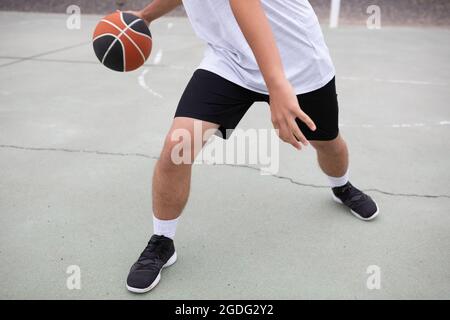 Männliche Jugendliche Basketballspieler Basketball spielen auf Gericht, Taille abwärts Stockfoto