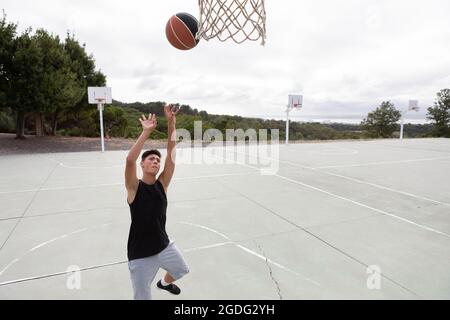 Männliche Jugendliche Basketballspieler wirft Ball in Richtung Basketballkorb Stockfoto