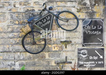 Nahaufnahme eines alten Herrenfahrrads, das an einer rustikalen Steinwand an den Schildern des Vintage-Souvenirshops La in der hügeligen, touristischen Main Street Haworth West Yorkshire, England, befestigt ist Stockfoto