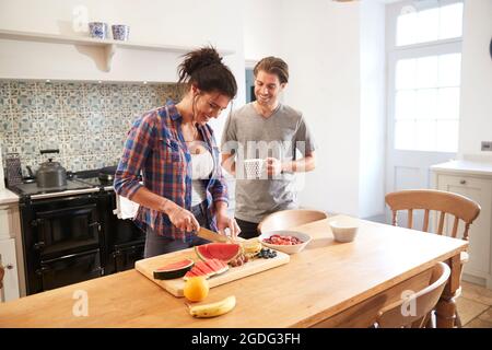 Paar schneiden frisches Obst und Chatten am Küchentisch Stockfoto