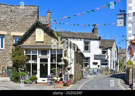 Bunting über schmalen Straße Grassington Dorf Straßenszene mit Blumenpflanzen Shop & Hotelgebäude am blauen Himmel Sommertag North Yorkshire England Großbritannien Stockfoto