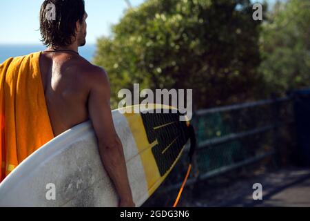 Mitte der erwachsenen männlichen Surfer, Surfbrett an der Beach Laufsteg, Rückansicht, Strand von Camps Bay, Kapstadt, Südafrika Stockfoto